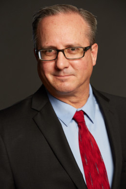 A man in glasses and a suit with red tie.