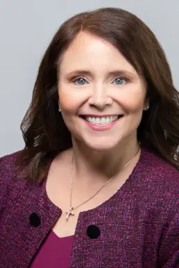 A woman with long brown hair wearing a purple shirt.